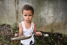 Criança com prato vazio segurando uma colher