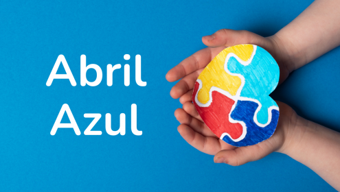 Mãos segurando um quebra-cabeças colorido em formato de coração, ao lado da frase "Abril Azul"