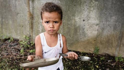 Criança com prato vazio segurando uma colher
