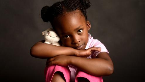 Criança sentada com pelúcia nos braços 